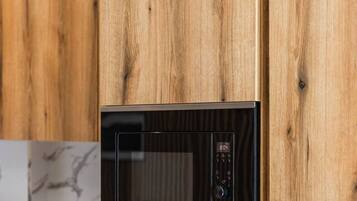 Una cocina con microondas y horno integrados, muebles de madera y un lavamanos de acero inoxidable.