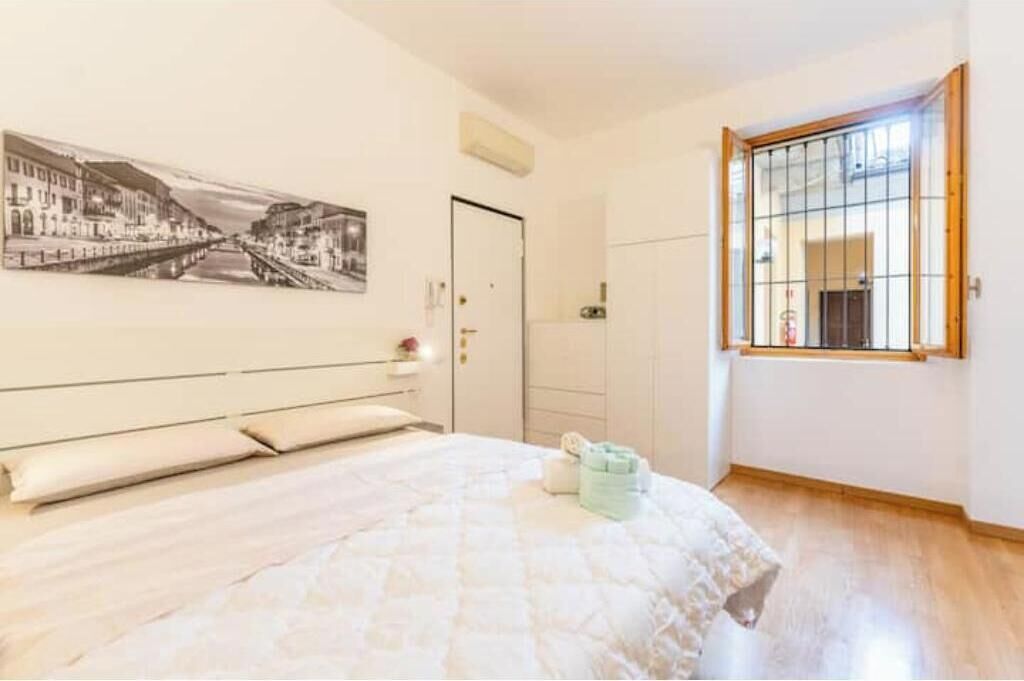 A bedroom with a bed, a window with bars, a door, and a wall-mounted picture.