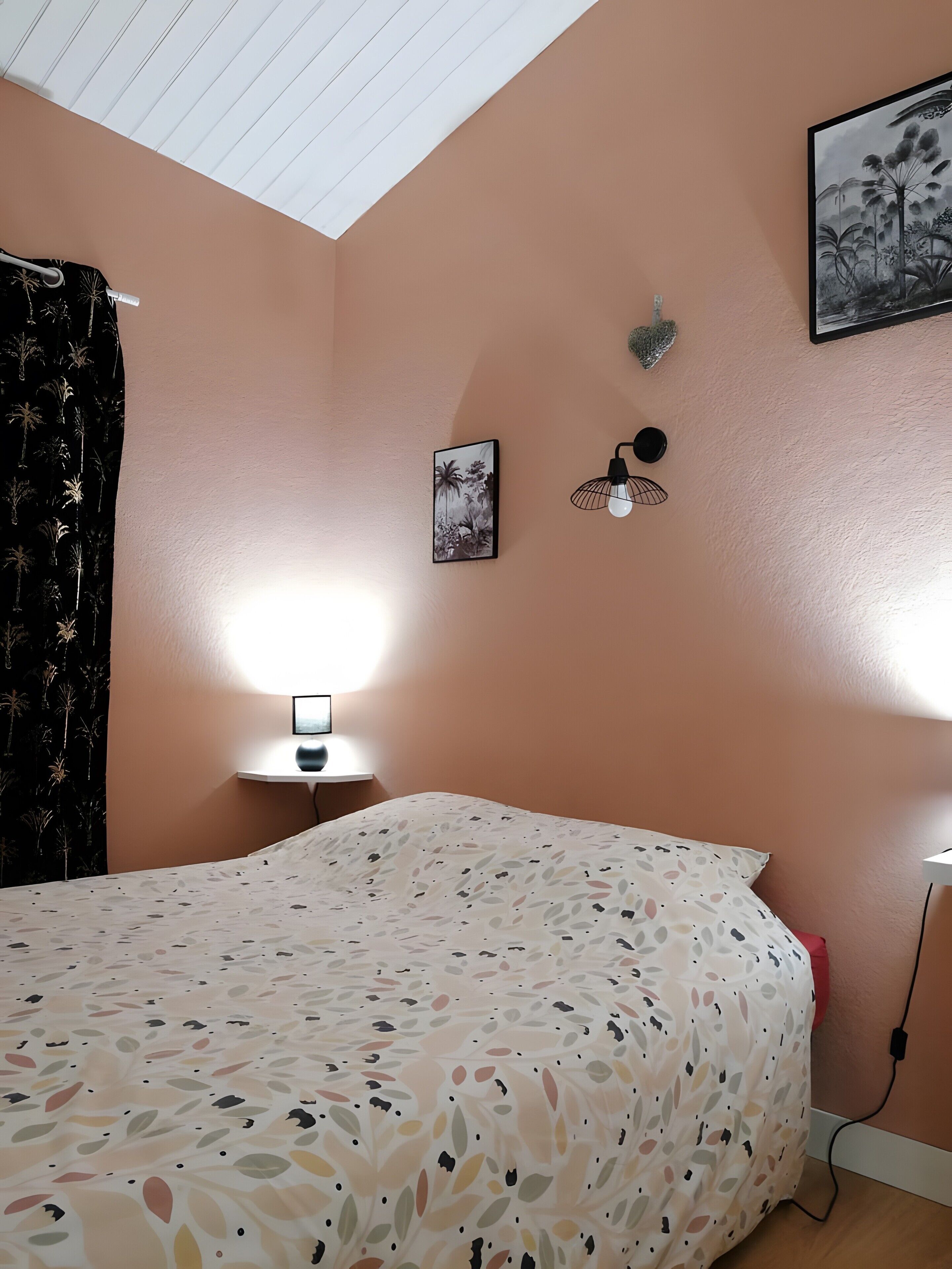 Een slaapkamer met een bed, een nachtkastje, een wandlamp, een lijst met een afbeelding en een plafondlamp.