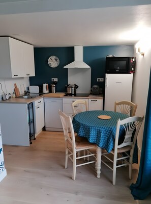 Eine kleine Küche mit weißen Schränken, einer Mikrowelle, einem Toaster und einem Tisch mit Stühlen.