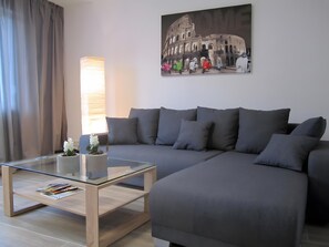 A modern living room with a sofa, a glass coffee table, a lamp, and a painting of the Colosseum.