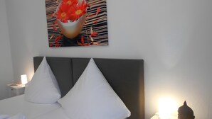 Ein ordentlich bezogenes Bett mit weißen Leinen, einem dunklen Kopfteil und einem an der Wand hängenden Blumenbild.
