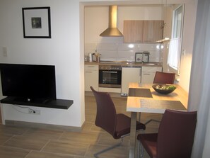 A modern kitchen with a TV, dining table, chairs, and a stove.