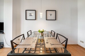 Una mesa de comedor con cuatro sillas, un florero con flores y dos cuadros en la pared.