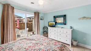 Ein Schlafzimmer mit Bett, Kommode, Fernseher und Blick ins Freie.