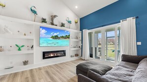 Ein Wohnzimmer mit Fernseher, Kamin und Blick auf einen tropischen Strand.
