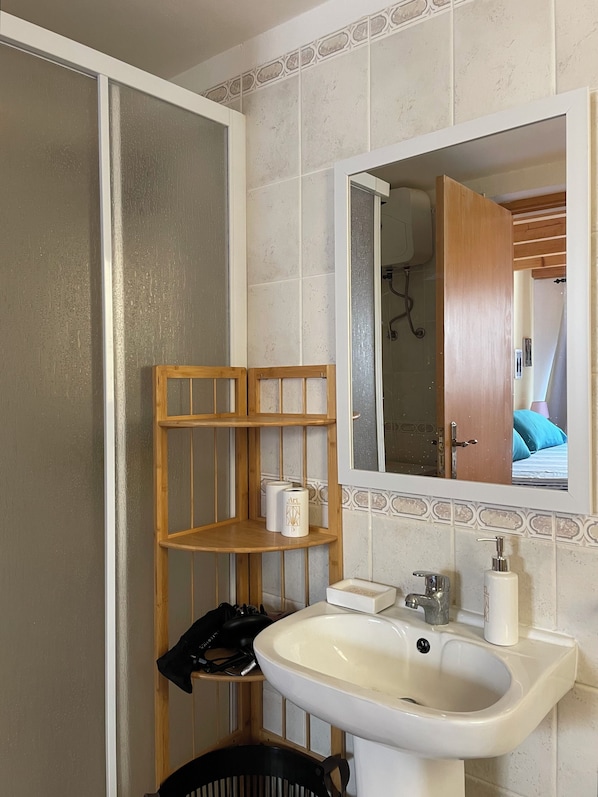 Une salle de bain avec un lavabo, un miroir et une étagère en bois où sont rangés les articles de toilette.