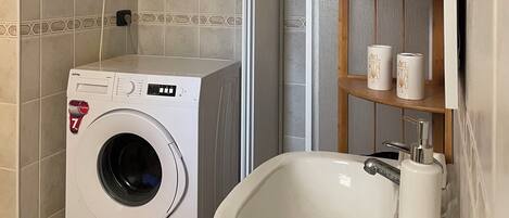 A washing machine, a sink, and a shelf with toiletry items in a bathroom.