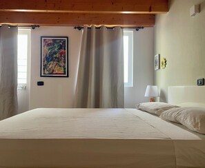 A bedroom with a bed, curtains, a painting, a nightstand, and a lamp. - Casetta Alida | Bright Central Loft with Starling & A/C (Santa Maria)