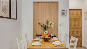 A dining table with white chairs, a fruit centerpiece, and framed artwork on the wall. - Prime Candolim 2bhk w Pool Near Beach Nightlife (Candolim)