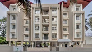 A multi-story residential building with balconies, a covered parking area, and a sign with palm tree symbols. - Prime Candolim 2bhk w Pool Near Beach Nightlife (Candolim)