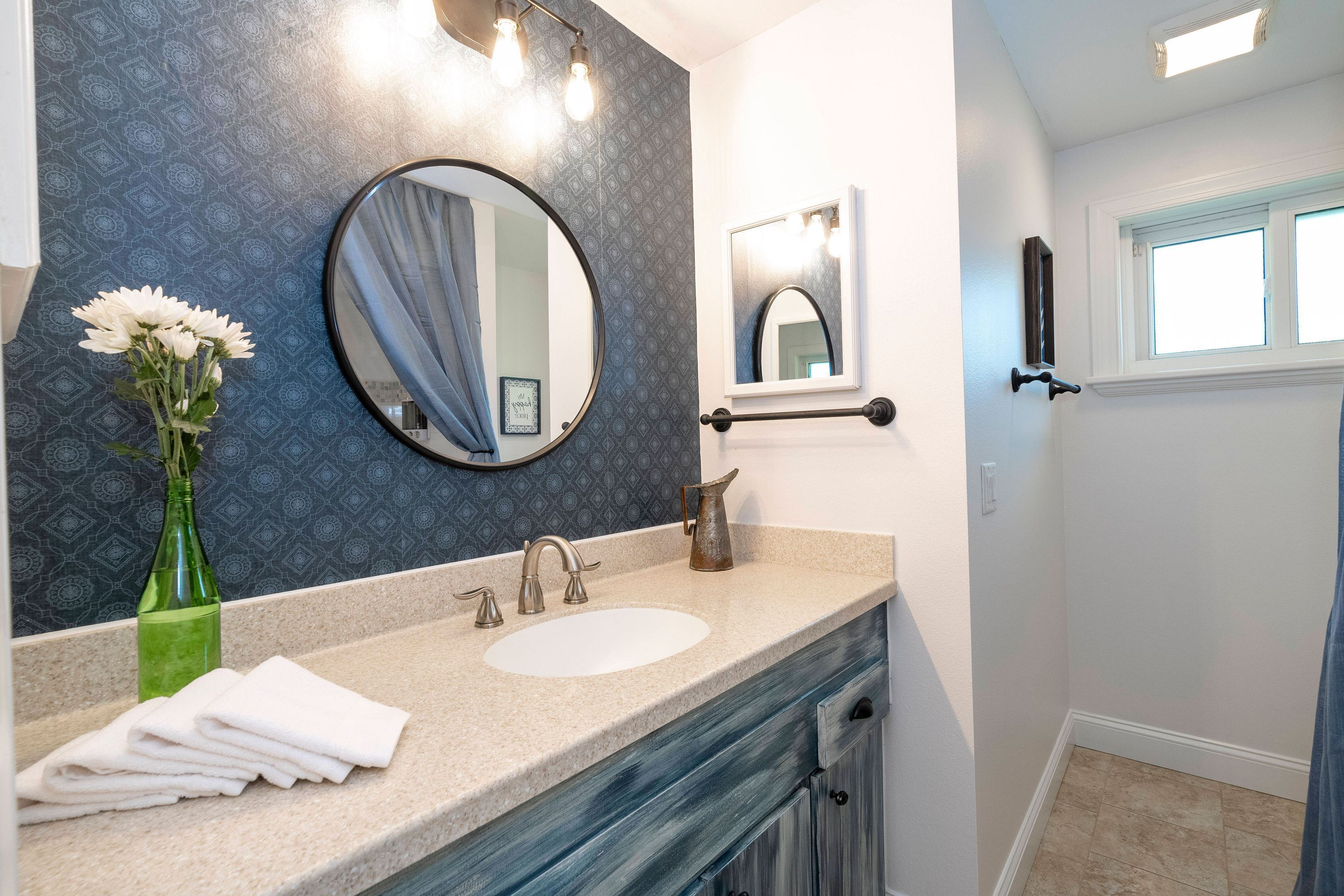 A bathroom with a vanity, sink, mirror, and towel stack.