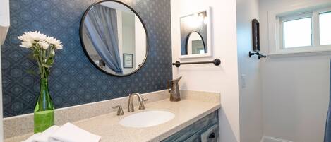 A bathroom with a vanity, sink, mirror, and towel stack.