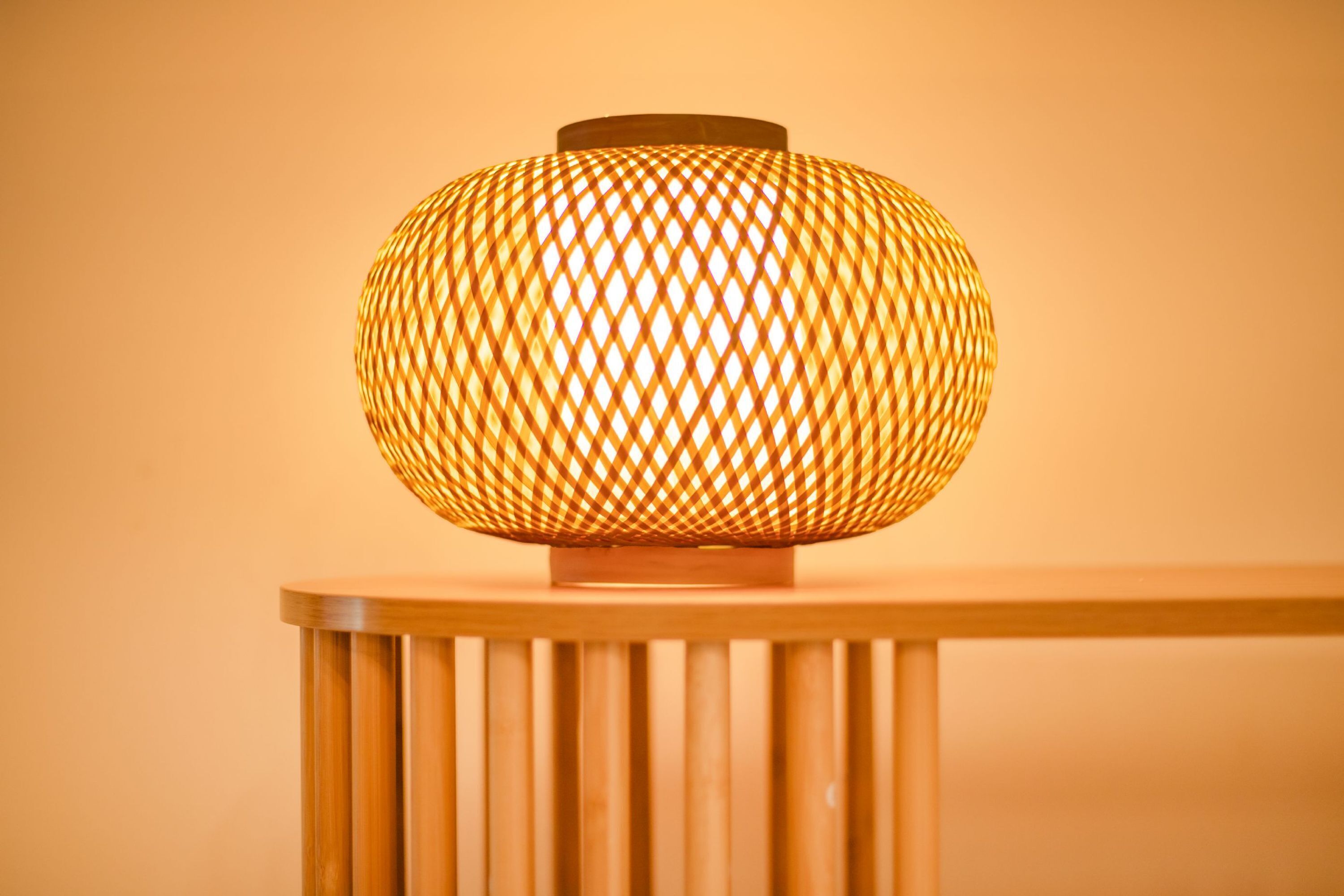A spherical lamp with a woven pattern on a wooden table against a plain background.