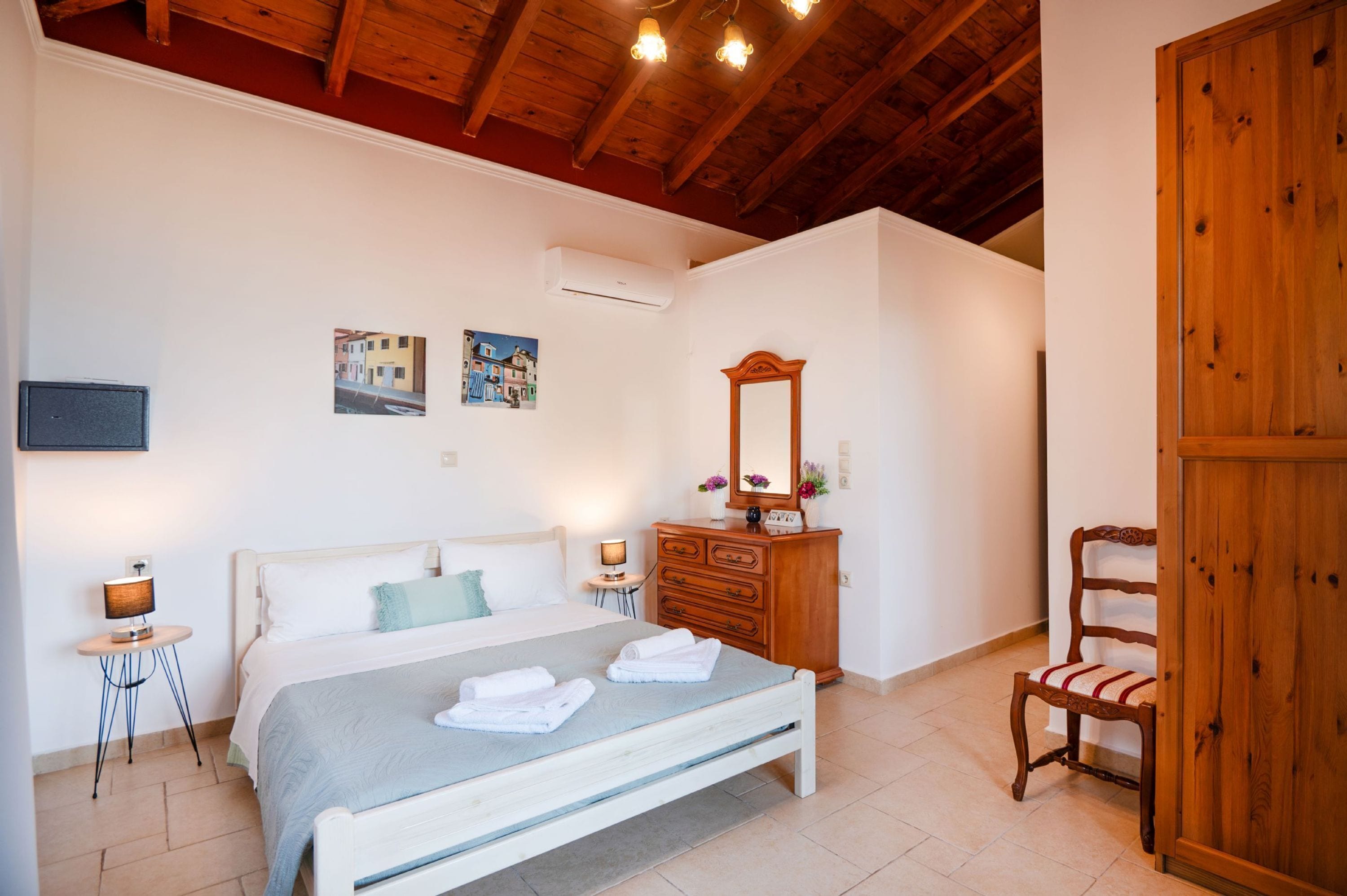 A bedroom with a bed, dresser, mirror, chair, and artwork on the wall.