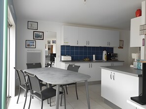 Ett modernt kök med vita skåp, ett blått stänkskydd och en matplats med ett bord och stolar i marmor.
