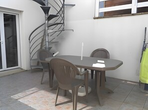 En uteplats med ett bord och stolar, en spiraltrappa och en skjutdörr i glas.