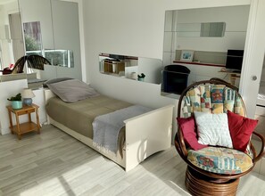 Ett modernt sovrum med en säng, ett sängbord med en lampa, en fåtölj med kuddar och en stor spegel.