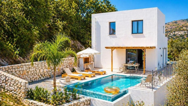 Eine moderne, weiße Villa mit Swimmingpool, Liegestühlen und einer Terrassenanlage.