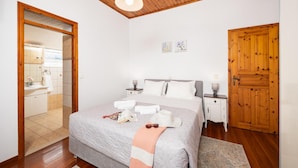 Ein Schlafzimmer mit Holzboden, einem Bett mit grauer Decke, zwei Nachttischen mit Lampen und einer Holztür.