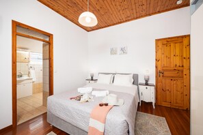 Ein Schlafzimmer mit Holzboden, einem Bett mit grauer Decke, zwei Nachttischen mit Lampen und einer Holztür.