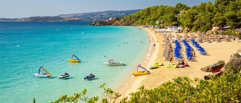 A beach with clear turquoise water, boats, and umbrellas.