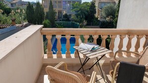 A balcony with wicker chairs, a small table, and a view of a swimming pool and buildings. - Villa El Olivo With 3 Bedrooms and 3 Bathrooms (Pollença)