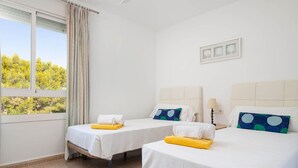 A hotel room with two beds, a window with curtains, a view of trees, and a wall-mounted picture. - Villa El Olivo With 3 Bedrooms and 3 Bathrooms (Pollença)