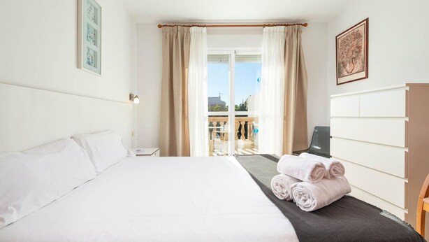 A hotel room with a bed, a desk, a chair, a TV, and a view of the outside. - Villa El Olivo With 3 Bedrooms and 3 Bathrooms (Pollença)