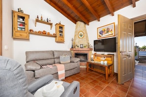 A living room with a sofa, television, fireplace, and wooden shelves. - Villa Cortijo Porroncico (Nerja)