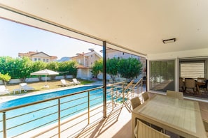 Un balcón con piscina, sillones de descanso y una zona de comedor con mesa y sillas.