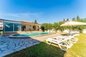 Una casa moderna con piscina, patio de piedra y mobiliario exterior.