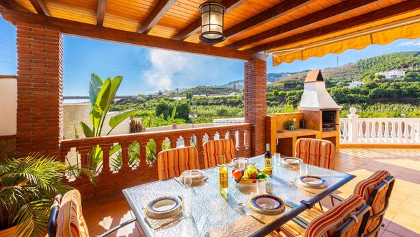 An outdoor patio with a table set for dining, surrounded by chairs, and a brick wall. - Villa Los Naranjos With 3 Bedrooms and 2 Bathrooms (Nerja)