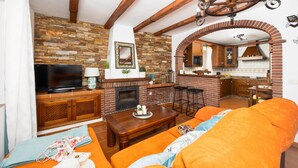 A living room with a fireplace, a television, and a kitchen area visible through an archway. - Villa Los Naranjos With 3 Bedrooms and 2 Bathrooms (Nerja)