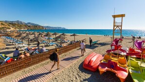 A beach with sun loungers, umbrellas, and a lifeguard tower. - Villa Los Naranjos With 3 Bedrooms and 2 Bathrooms (Nerja)