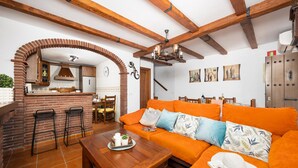 A cozy living area with a wooden bench, orange sofa, and a brick archway leading to a kitchen. - Villa Los Naranjos With 3 Bedrooms and 2 Bathrooms (Nerja)