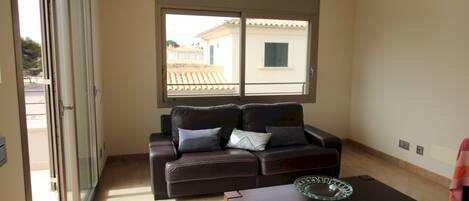 A living room with a brown leather sofa, a glass coffee table, and a sliding glass door leading to an outdoor area.