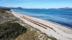Ein Küstenstrand mit Holzzaun, einer kleinen Brücke und freiem Blick auf das Meer und ferne Berge.
