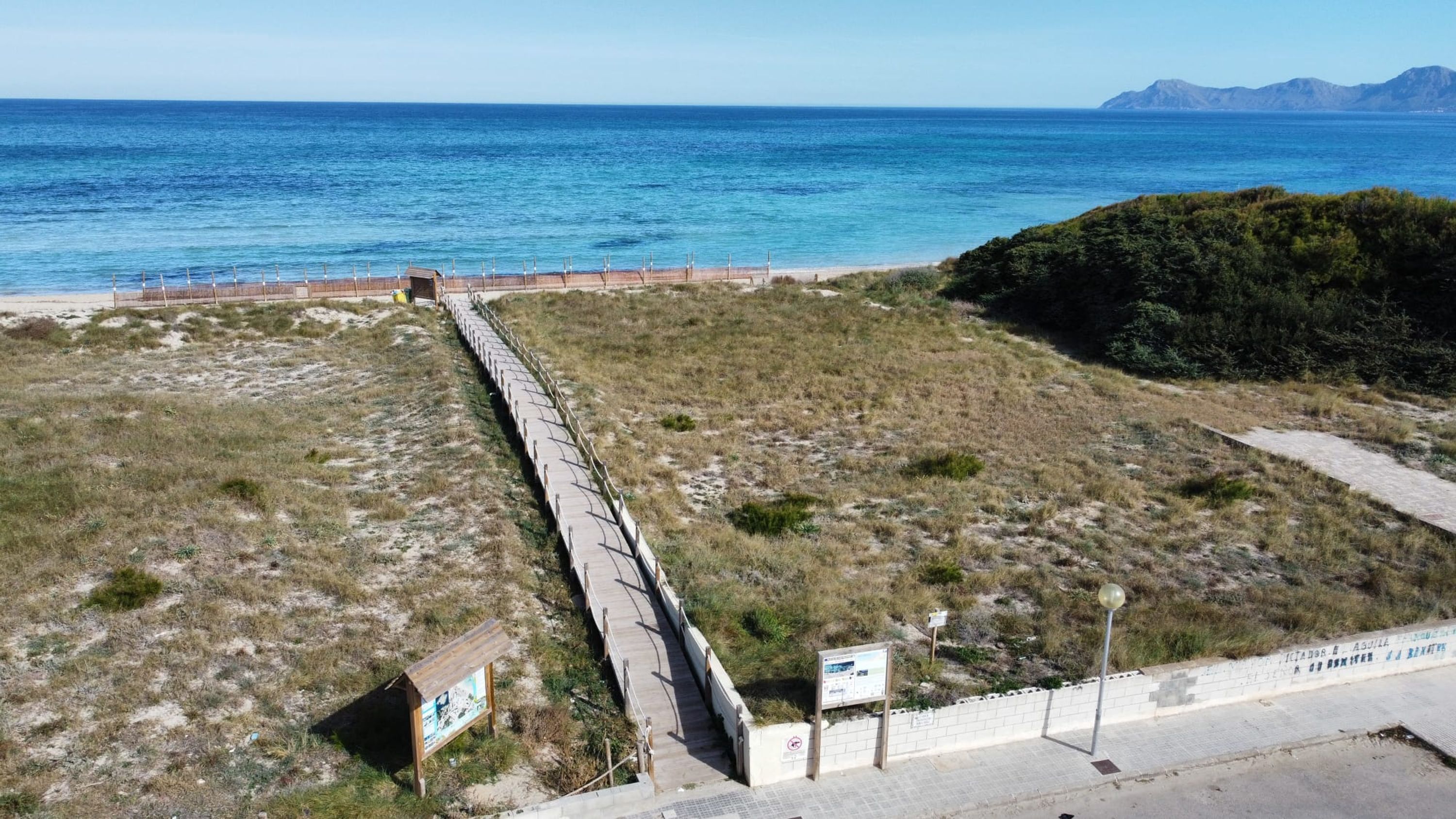 A coastal landscape with a paved walkway, grassy areas, and a beach.