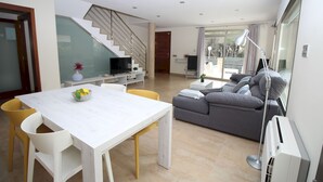 Ein modernes Wohnzimmer mit einem weißen Esstisch, gelben Stühlen, einem grauen Sofa und einer Treppe, die zu einer weiteren Ebene führt.