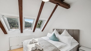 A bedroom with a sloped ceiling, skylights, a bed with pillows, a bedside table, and a radiator. - Ramoni Apartments - Enzzauber - Bad Wildbad (Bad Wildbad)