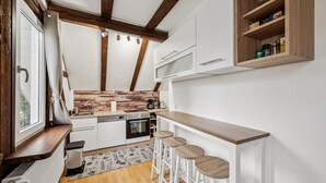 A modern kitchen with wooden beams, white cabinetry, a built-in oven, and a bar area with stools. - Ramoni Apartments - Enzzauber - Bad Wildbad (Bad Wildbad)