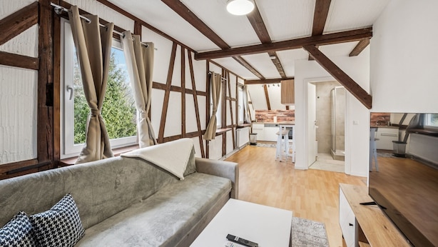 A modern interior with exposed wooden beams, a sofa with patterned pillows, a white coffee table, and a kitchen area in the background. - Ramoni Apartments - Enzzauber - Bad Wildbad (Bad Wildbad)