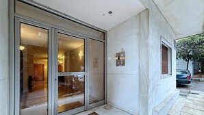 Entrada de un edificio con puerta de vidrio, felpudo y placa metálica en la pared.