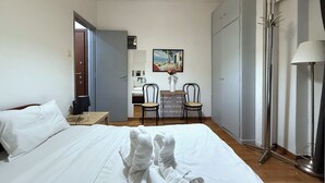 Habitación de hotel con cama, escritorio, dos sillas, un cuadro y una lámpara de pie.
