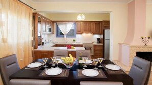 A dining area with a table set for four, a kitchen in the background, and a fireplace with candles. - Sunrise Villa With 3 Bedrooms and 3 Bathrooms (Kefalonia)