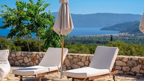 A terrace with two lounge chairs and an umbrella, overlooking a scenic landscape with a lake and mountains. - Sunrise Villa With 3 Bedrooms and 3 Bathrooms (Kefalonia)