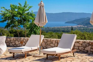 Eine Terrasse mit zwei Liegestühlen und einem Sonnenschirm, mit Blick auf eine malerische Landschaft mit See und Bergen.