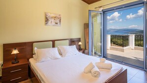 A bedroom with a bed, bedside lamps, a painting, and a balcony with a view. - Sunrise Villa With 3 Bedrooms and 3 Bathrooms (Kefalonia)