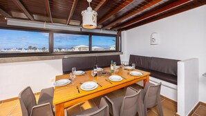 Ein Essbereich mit Holztisch, gedeckt für vier Personen, einer Couch und Blick auf das Meer.